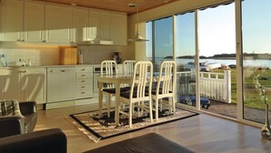 Eine moderne Küche mit weißen Schränken und einem Essbereich mit Tisch und Stühlen. Ein großes Fenster bietet Blick auf einen See und Boote.