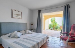 A bedroom with a bed, a chair, a lamp, and a view of the garden through an open door. - Lovely home in Sainte-Maxime with WiFi (Sainte-Maxime)