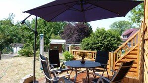 Une terrasse extérieure avec une table et des chaises, un grand parasol et une plateforme en bois.