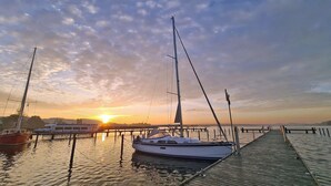 Un port de plaisance avec des bateaux amarrés, une jetée en bois et un coucher de soleil en arrière-plan.