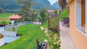 Un balcone con vista su un campo verde e montagne, un piccolo giardino fiorito e un tavolo con sedie.