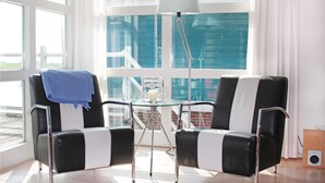 Una habitación moderna con dos sillas a rayas negras y blancas, una mesita de cristal con una vela, y un ventanal con vistas a edificios.