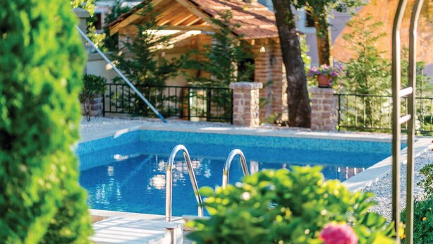 A swimming pool with clear blue water, surrounded by greenery and a brick building in the background. - Awesome apartment in Herceg Novi (Herceg Novi)