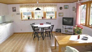 A cozy room with a wooden dining table, chairs, a television, and a kitchen area with a sink and cabinets.