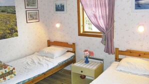 A bedroom with two single beds, a small bedside table with a lamp, and a window with curtains.