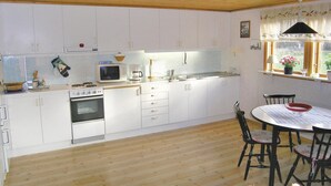 A kitchen with white cabinets, a stove, a microwave, and a sink. There is a dining table with chairs and a window with curtains.