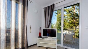 A living room with a television on a white stand, a red vase, and a sliding glass door leading to an outdoor area with a table and chairs.