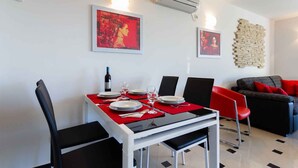 A dining area with a table set for four, two chairs on each side, a red placemat, and a bottle of wine.