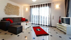A modern living room with a sofa, ottoman, coffee table, and a flat-screen TV on a stand.