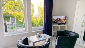 Ett modernt vardagsrum med en matplats, en tv och utsikt över en trädgård.