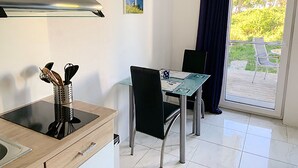 Ett litet kök med en spis, ett handfat och en matplats med ett bord och stolar. Det finns ett fönster med utsikt över grönområden utanför.