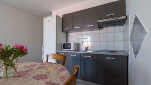 Une cuisine compacte équipée d’un four à micro-ondes, d’un réfrigérateur et de meubles de rangement de couleur sombre. On y trouve une table à manger recouverte d’une nappe à motifs floraux et agrémentée d’un vase rempli de fleurs.