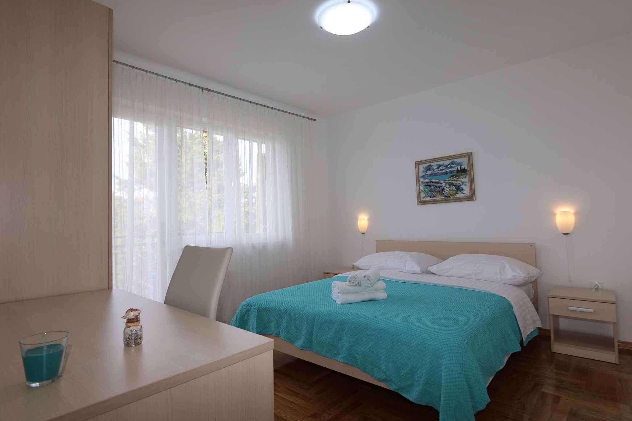 A hotel room with a bed, a desk, a chair, a nightstand, and a painting on the wall.
