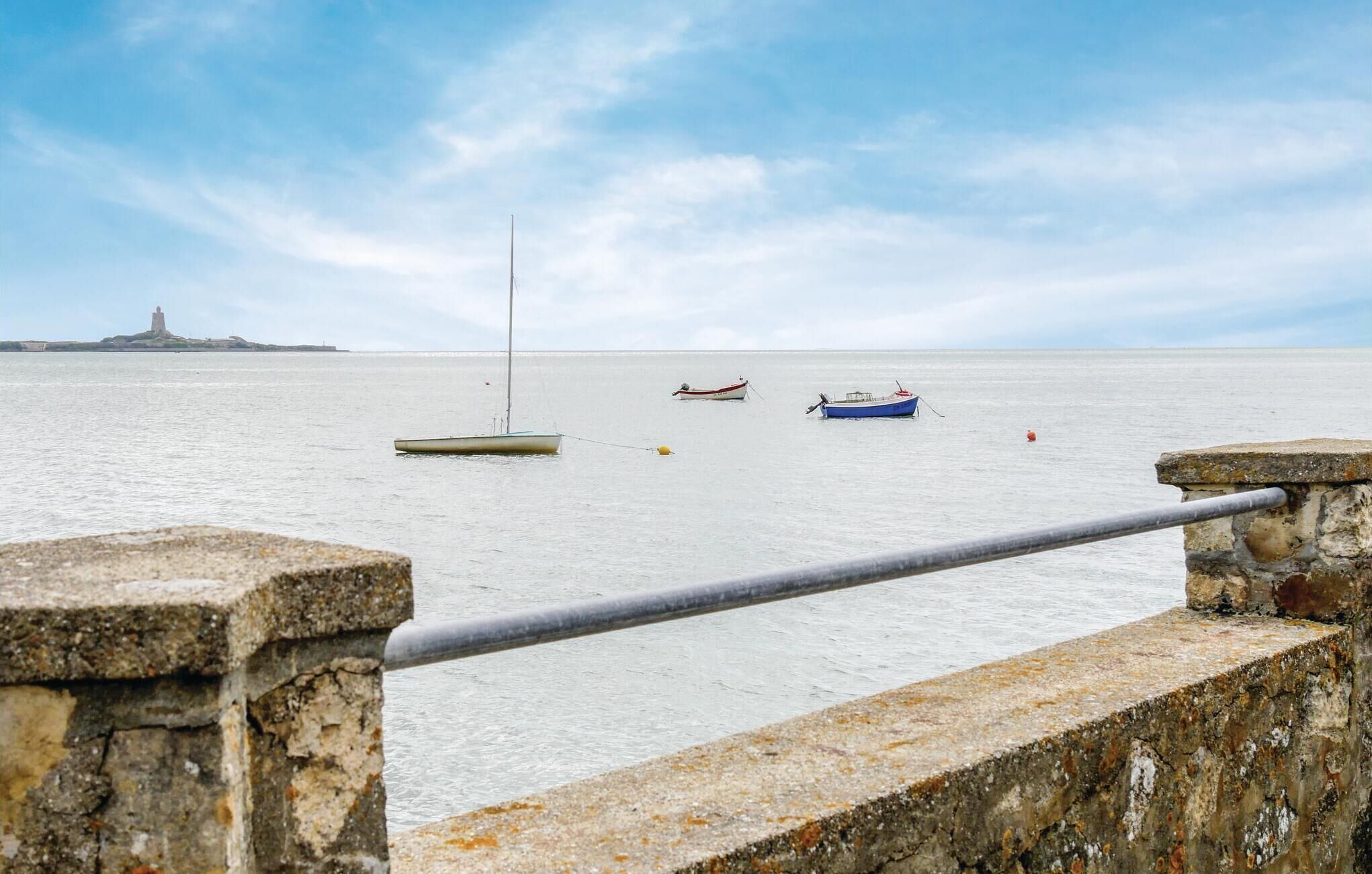 Een kustlandschap met een stenen balustrade, een rustige zee en een verafgelegen vuurtoren.