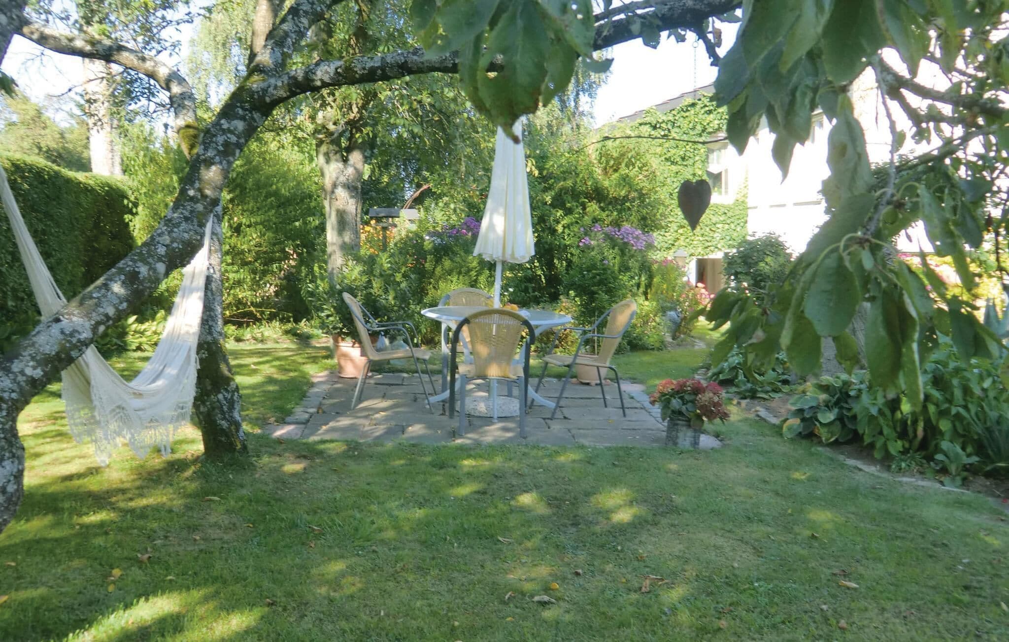 Eine Gartenpatio mit Tisch und Stühlen, umgeben von üppigem Grün und einer Hängematte.