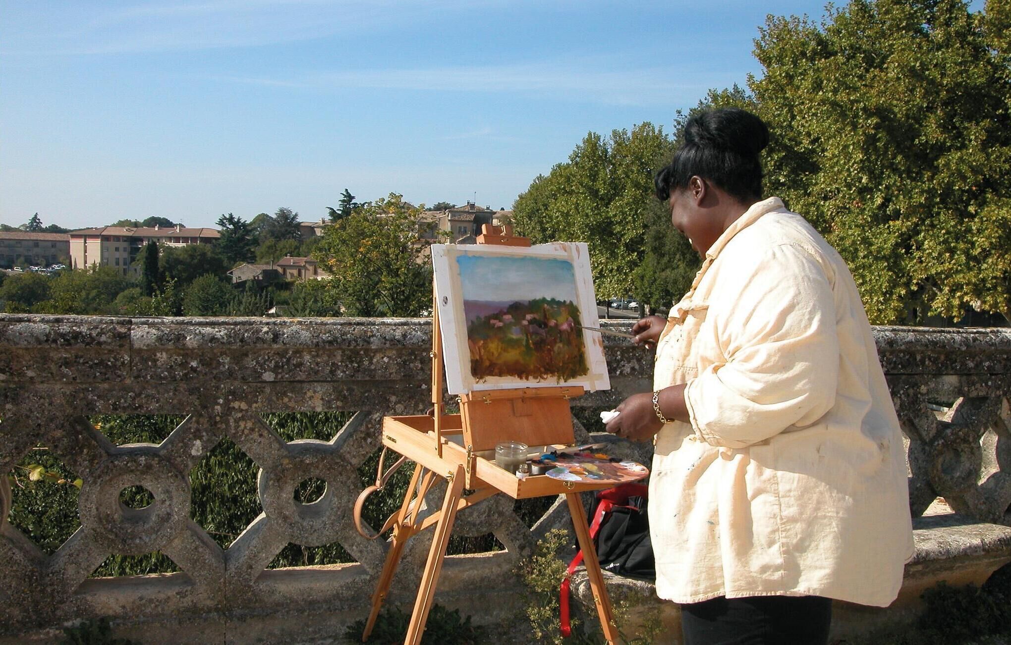 Una persona dipinge su un cavalletto con vista su un paesaggio sullo sfondo.