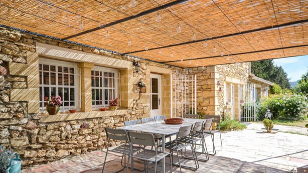 Eine Außenpatio mit einer Steinmauer, einem Tisch mit Stühlen und einer Pergola mit hängenden Lichtern.