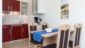 A compact kitchen with wooden cabinets, a dining table with chairs, and a coffee machine. - Apartment Perlmuschel - Holiday Apartment Perlmuschel (Esens)