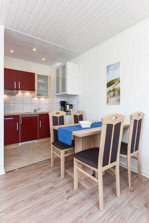 Une cuisine compacte avec des meubles de rangement en bois, une table à manger avec des chaises et une machine à café.