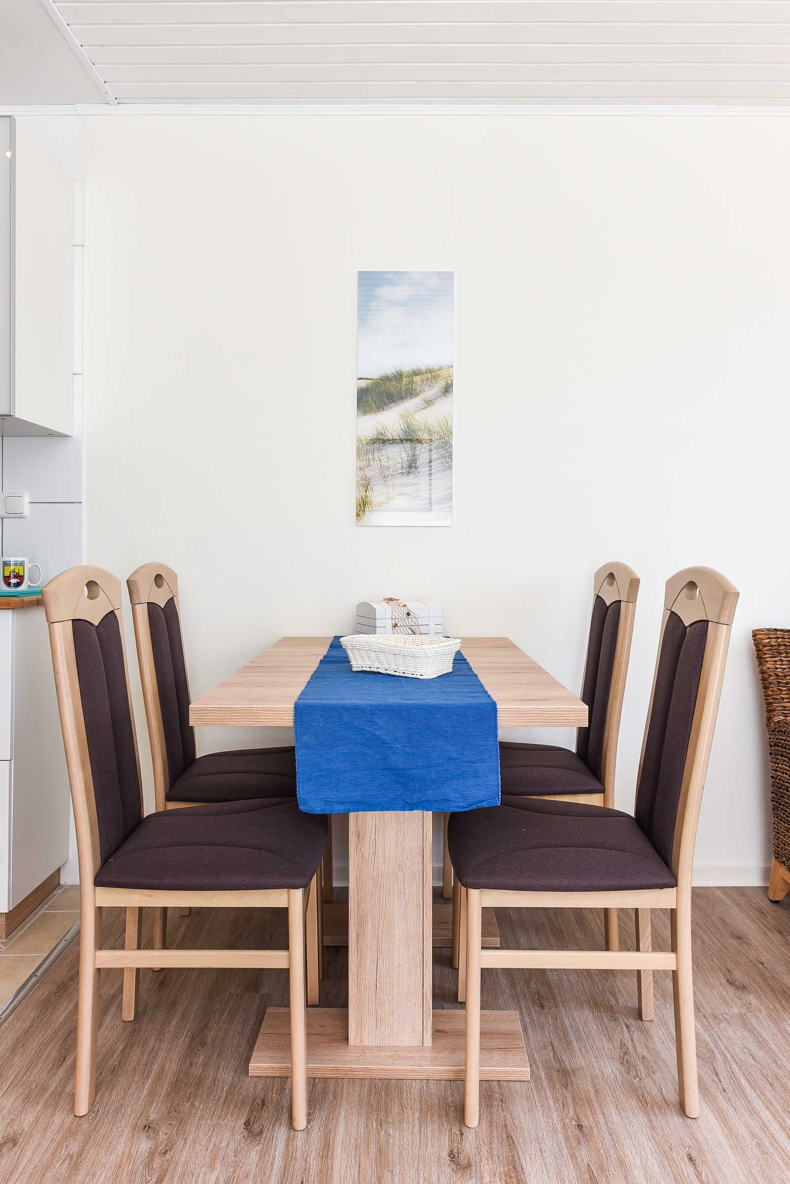 Ein Essbereich mit einem Holztisch, vier Stühlen, einer blauen Tischdecke und einem gerahmten Bild an der Wand.