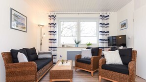 A living room with wicker furniture, a television, and a window with curtains. - Apartment Perlmuschel - Holiday Apartment Perlmuschel (Esens)