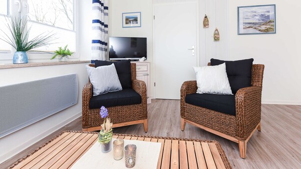 A room with two wicker sofas, a TV, and a window with curtains. - Apartment Perlmuschel - Holiday Apartment Perlmuschel (Esens)