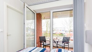 A bedroom with a bed, a sliding glass door leading to a balcony with two chairs and a table. - Apartment Perlmuschel - Holiday Apartment Perlmuschel (Esens)