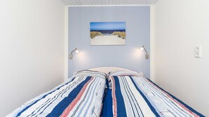 A bedroom with a bed featuring striped bedding, a painting of a beach scene on the wall, and two bedside lamps. - Apartment Perlmuschel - Holiday Apartment Perlmuschel (Esens)