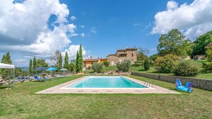 A swimming pool with lounge chairs and umbrellas, surrounded by a grassy area and a stone building in the background. - Beautiful home in Città´di Castello -PG- (Città´di Castello -PG-)