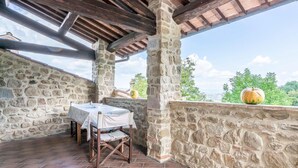 A stone-walled outdoor patio with a table and chairs, a stone pillar, and a view of greenery. - Beautiful home in Città´di Castello -PG- (Città´di Castello -PG-)