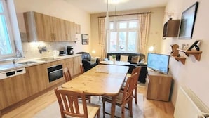 Une cuisine compacte avec des meubles en bois, une table à manger avec des chaises, un petit coin salon avec un canapé et un téléviseur posé sur un meuble.