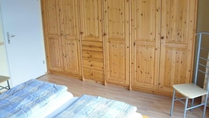 Une pièce comprenant une grande armoire en bois, un lit recouvert d’une couverture à rayures et une chaise en métal.