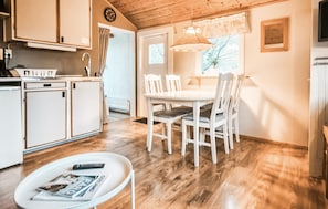 Een keuken met witte kasten, een eettafel met stoelen, een klein rond tafeltje met een tijdschrift, en een hanglamp.