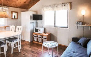 Een gezellige, compacte keuken met een eettafel, stoelen, een magnetron, een klein kastje, een televisie en een bank.