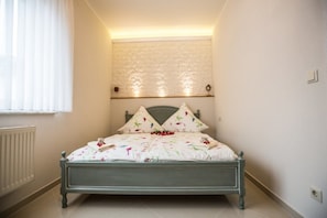 A bedroom with a bed, a window with blinds, a radiator, and a textured wall above the bed.