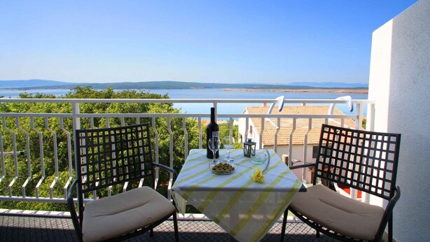 A balcony with a table set for two, a bottle of wine, and a bowl of olives. - Holiday apartment with balcony and air conditioning (Dramalj)