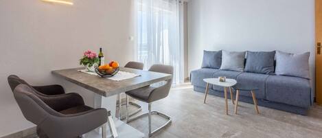 A modern living room with a grey sofa, a dining table with chairs, and a small side table.