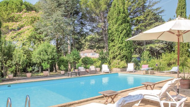 A swimming pool with lounge chairs and umbrellas, surrounded by trees and a house in the background. - Stunning home in Lançon de Provence (Lançon de Provence)