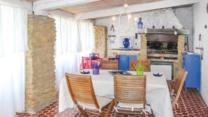 A rustic dining area with a stone wall, wooden ceiling, and a tiled floor. There is a table with chairs, a chandelier, and a blue cabinet. - Stunning home in Lançon de Provence (Lançon de Provence)