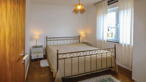 Une chambre à coucher avec un lit, des tables de chevet, une lampe, une fenêtre avec des rideaux et une porte en bois.