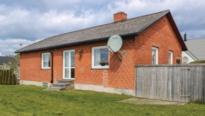 Une maison en briques rouges, avec une antenne parabolique, une clôture en bois et une cour gazonnée.