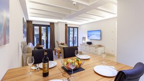 Une salle à manger moderne avec une table en bois dressée pour quatre personnes, un téléviseur accroché au mur et une vue sur l’extérieur grâce à de grandes fenêtres.