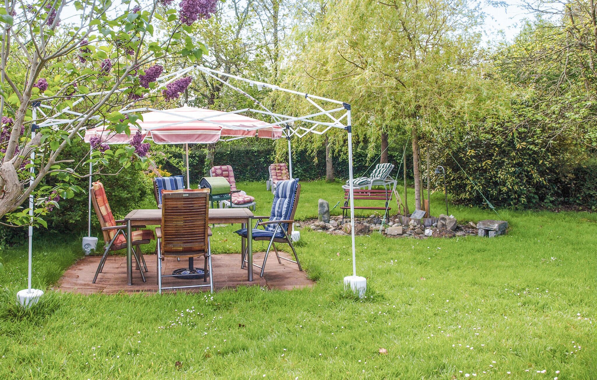 Un patio al aire libre con una mesa y sillas, rodeado de abundante vegetación y un toldo blanco.