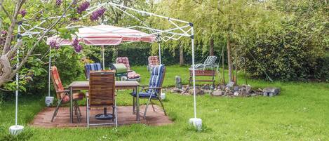 Un patio al aire libre con una mesa y sillas, rodeado de abundante vegetación y un toldo blanco.