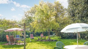 A garden with a table and chairs, a swing set, and a picnic table under a striped umbrella. - 2 bedroom lovely home in Pleubian (Pleubian)