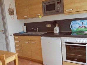 Una cocina compacta con armarios de madera, microondas, pileta, lavavajillas y horno.