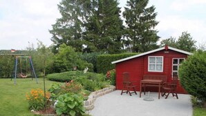 Una casa di legno rossa con un patio, immersa in un giardino con un'altalena.
