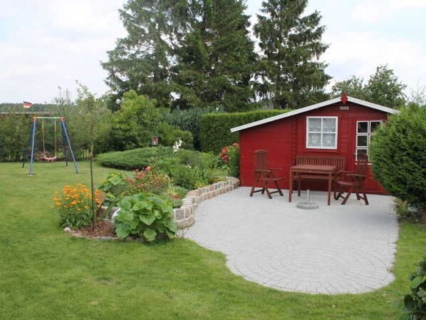 Una casa de madera roja con un patio, rodeada por un jardín con un columpio.