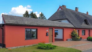 Un edificio rosso con tetto di paglia, un piccolo portico e un prato ben curato.