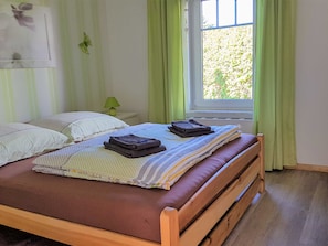 Una cama bien hecha con almohadas y toallas dobladas, una lámpara de noche y una ventana con cortinas.